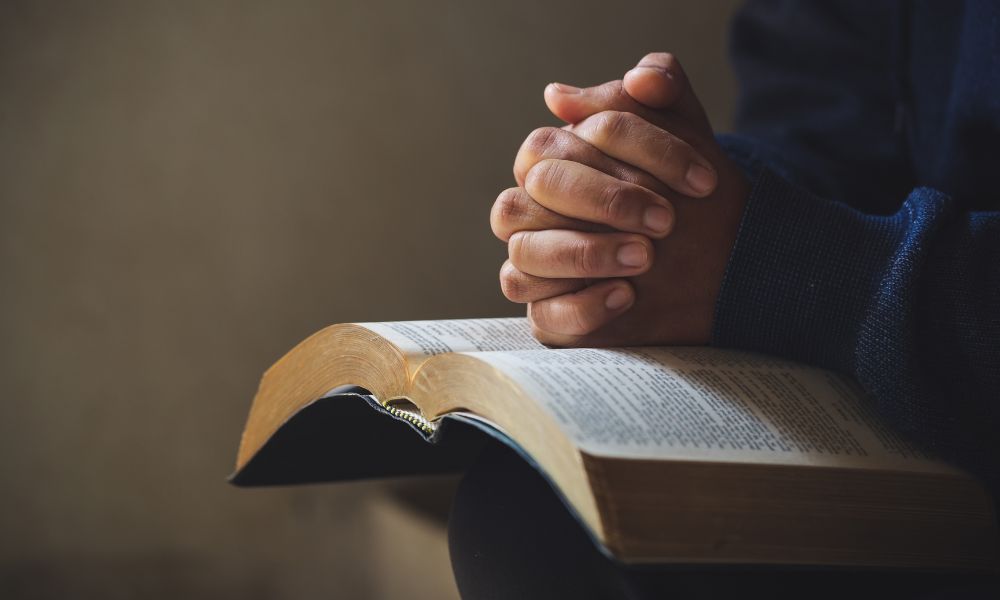 Hands clasped in prayer over an open book