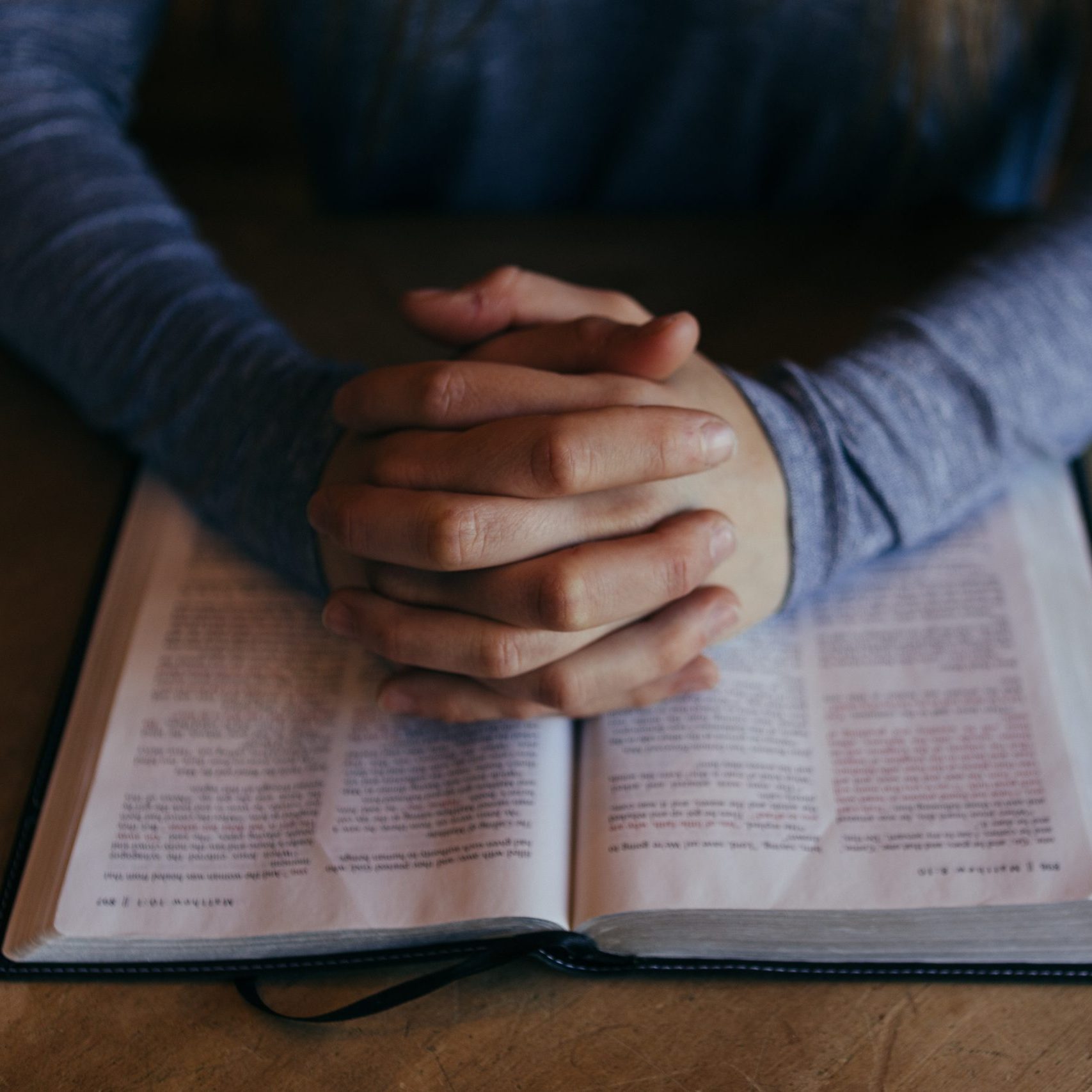 Hands clasped in prayer over Bible